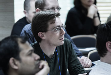 Group of people listening in a classroom with focus on a student with glasses in the center