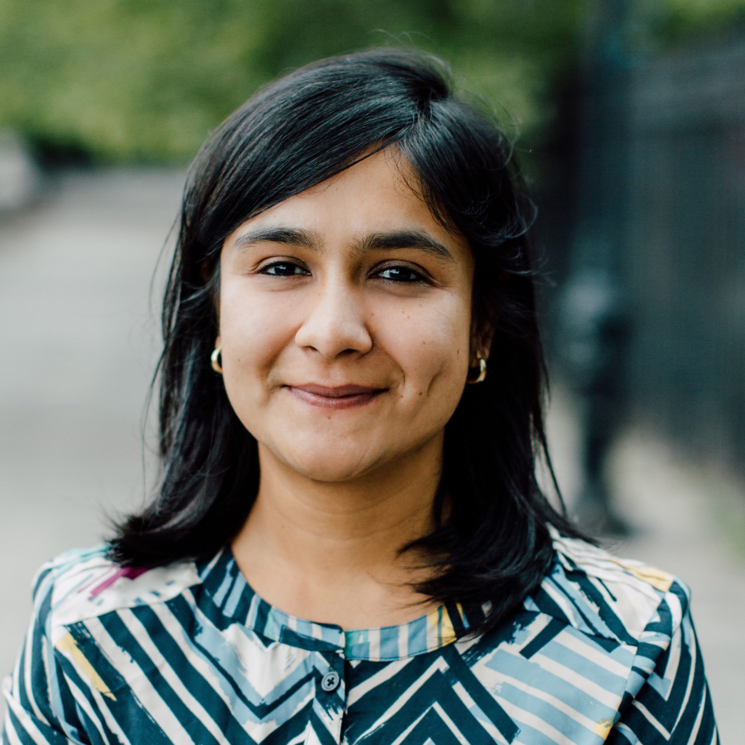 Romita Mitra – a woman with light brown skin looking outside, looking at the camera and smiling